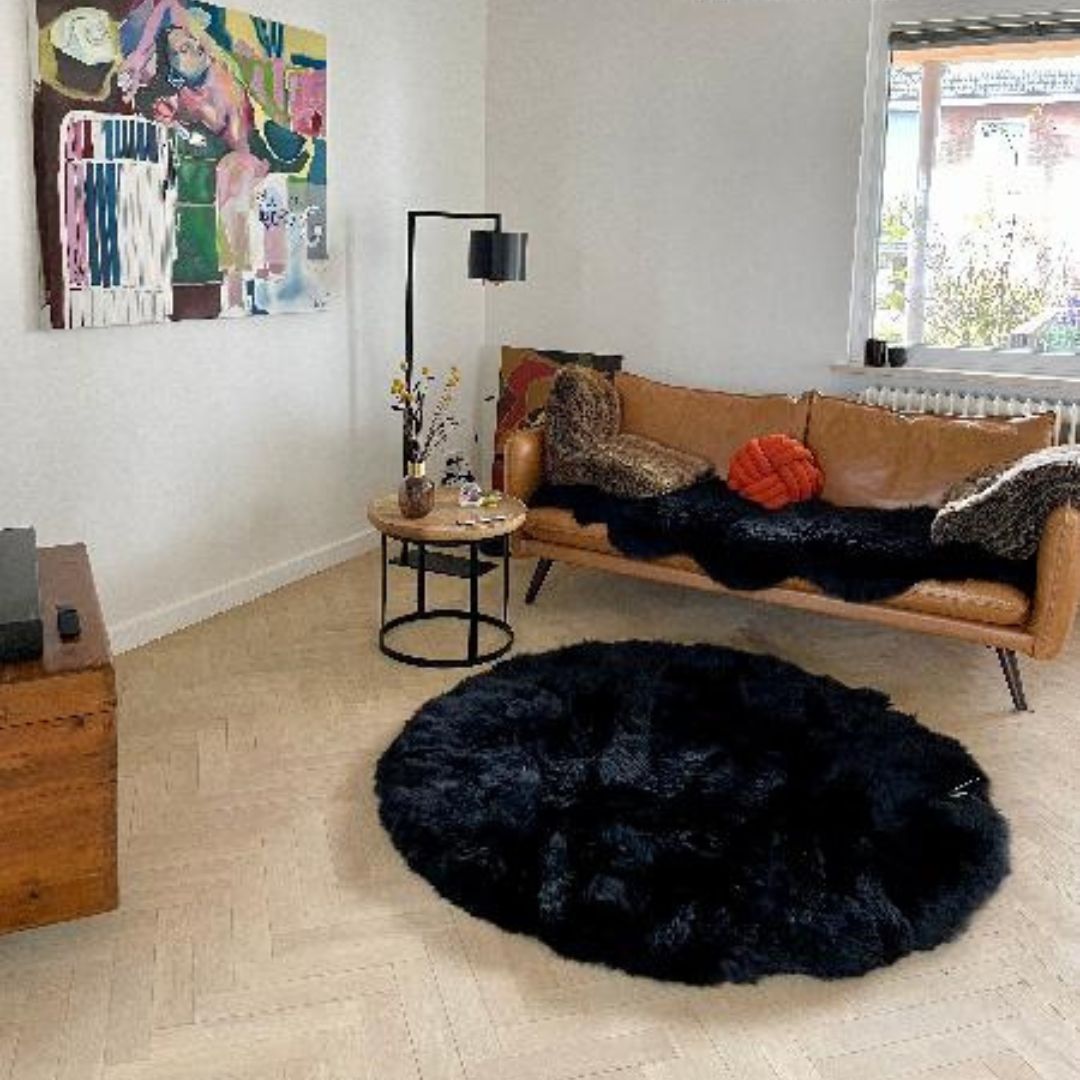 Runder schwarzer Lammfellteppich vor Ledersofa im modernen Wohnzimmer - Lammfell als runder Teppich für stilvolles Wohnambiente