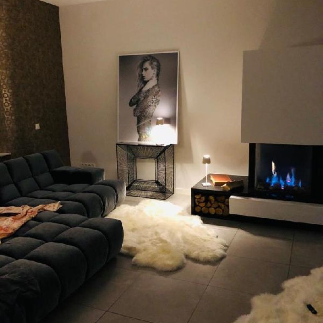 Großer weißer Lammfellteppich vor Kamin im modernen Wohnzimmer mit Sofa - Lammfell als Teppich für gemütliches Wohnambiente