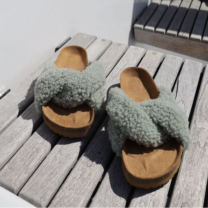 Lammfell Sandalen in Salbeigrün auf Holzbank - bequeme Damen-Pantoletten aus echtem Lammfell für den Sommer