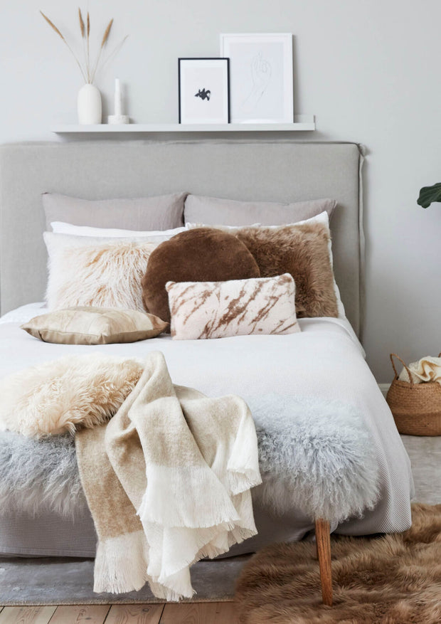 Fellkissen in verschiedenen Grössen und Wolldecke auf einem Bett