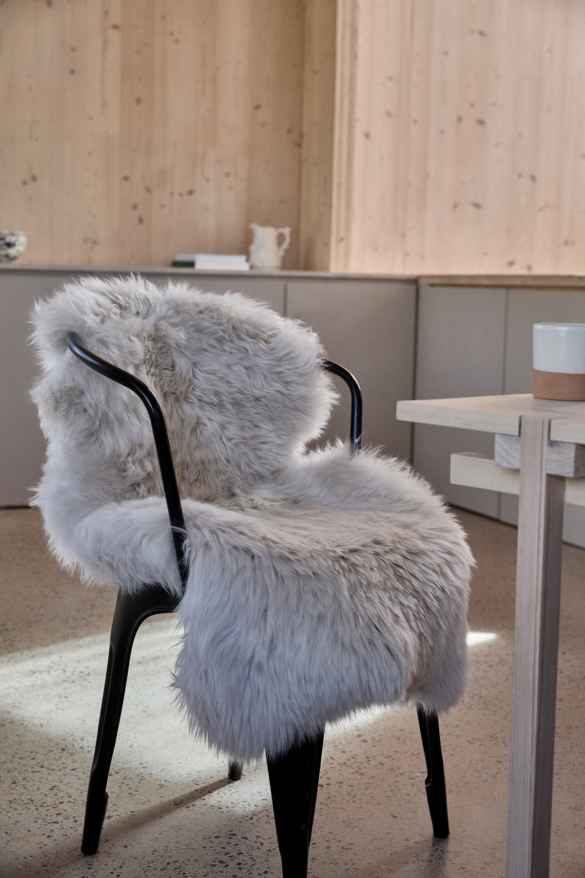 Weißes langhaariges Lammfell auf schwarzem Designer-Stuhl - elegantes Lammfell für Stühle in modernem Wohnambiente